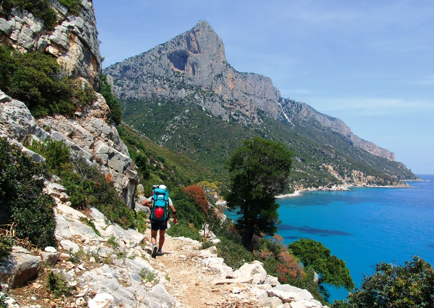 Randonneur sur sentier escarpé dominant crique turquoise